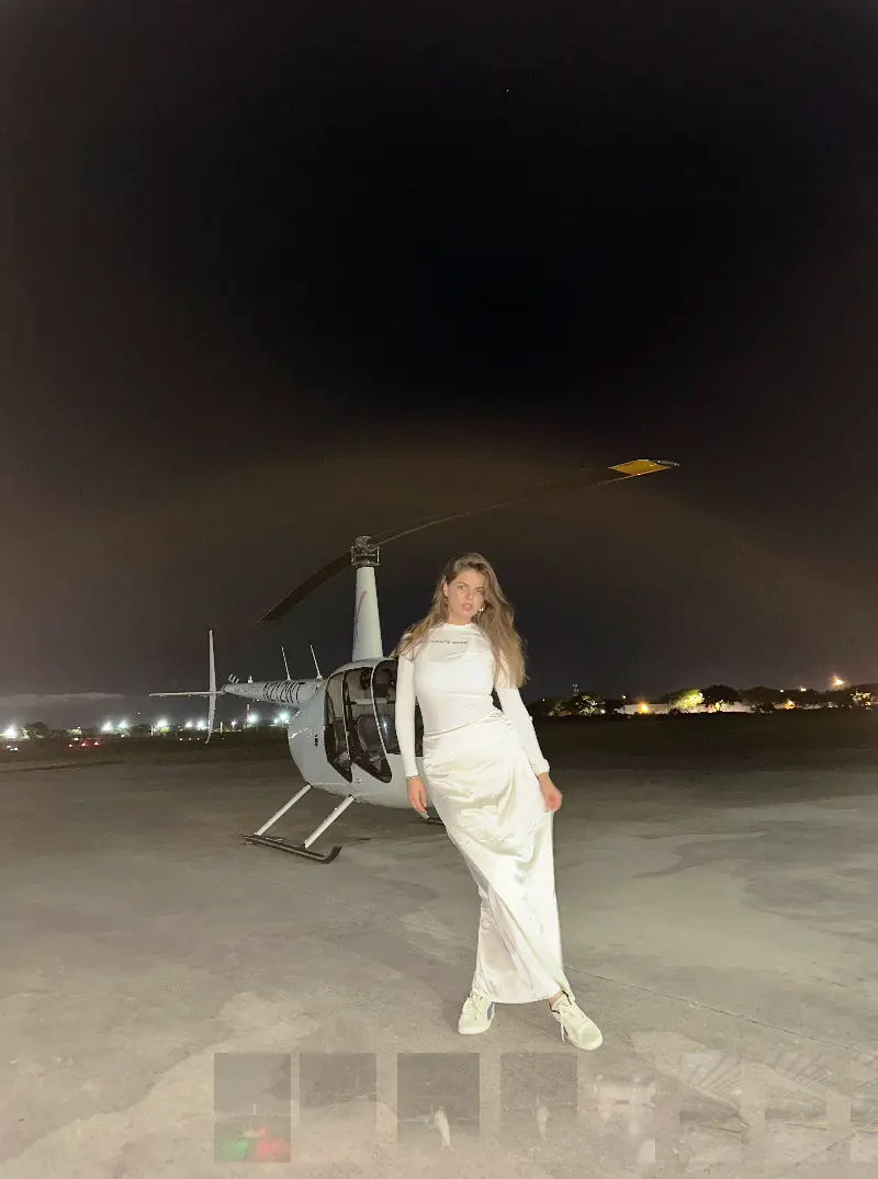 Maria standing by a white Robinson helicopter on the tarmac at night